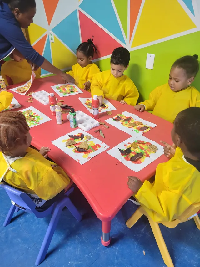 Des enfants en tabliers jaunes colorient des feuilles d'automne autour d'une table