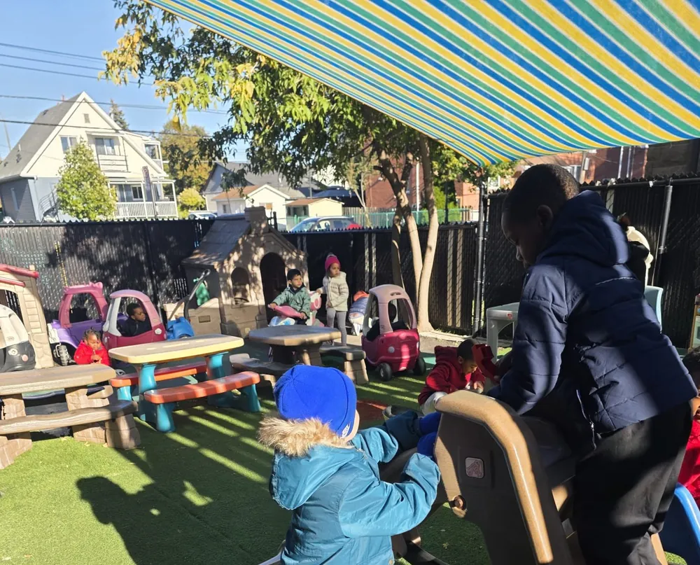 Des enfants en manteaux d'automne jouent sur la glissade de la cour, sous un auvent rayé