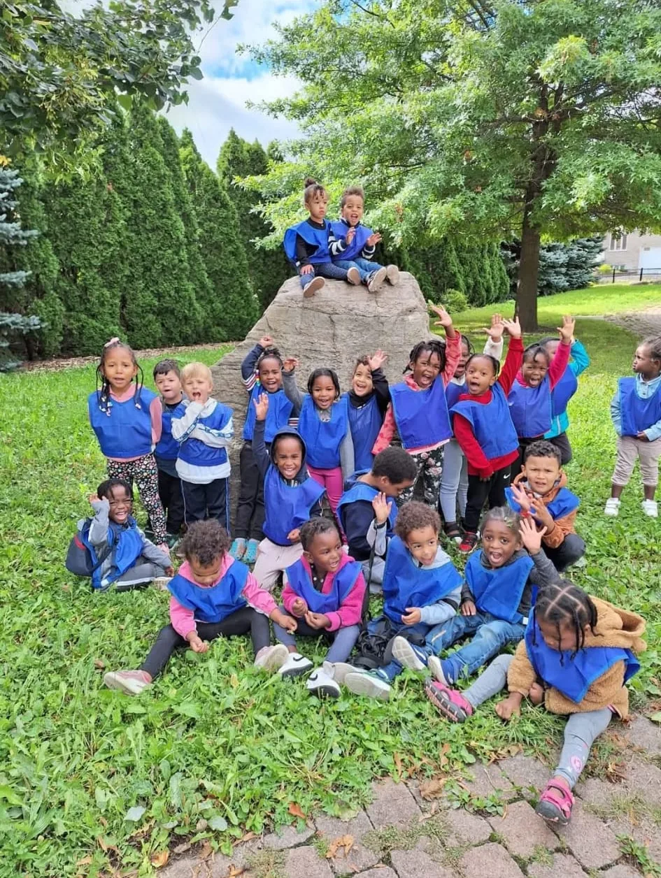 Les enfants de la garderie, en dossards bleus, posent tout sourire autour d'un rocher au parc