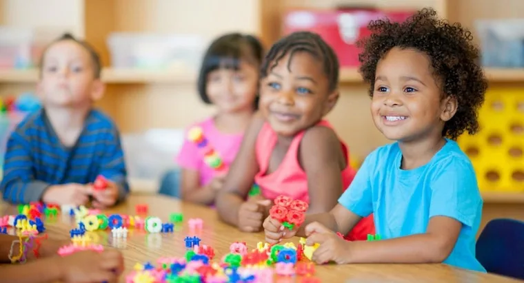 Des tout-petits souriants jouent avec des jeux de construction autour d'une table